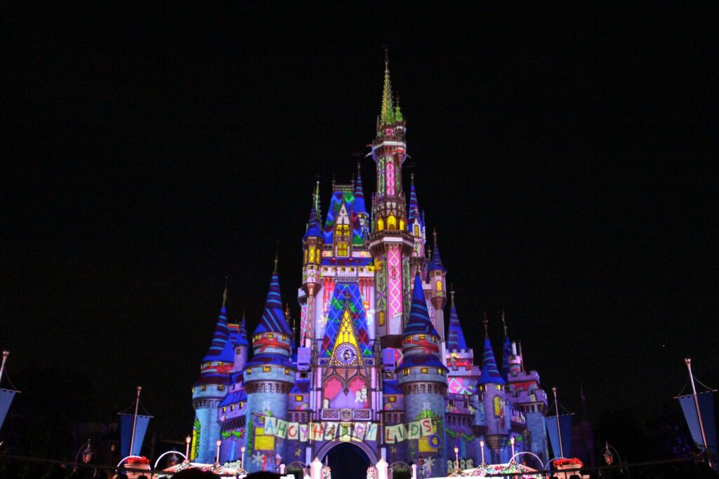 A colorful Cinderella Castle at Magic Kingdom glows with the message "Ahoy happy lids" during the Frozen Holiday Surprise stage show at Mickey's Very Merry Christmas Party at Disney World.
