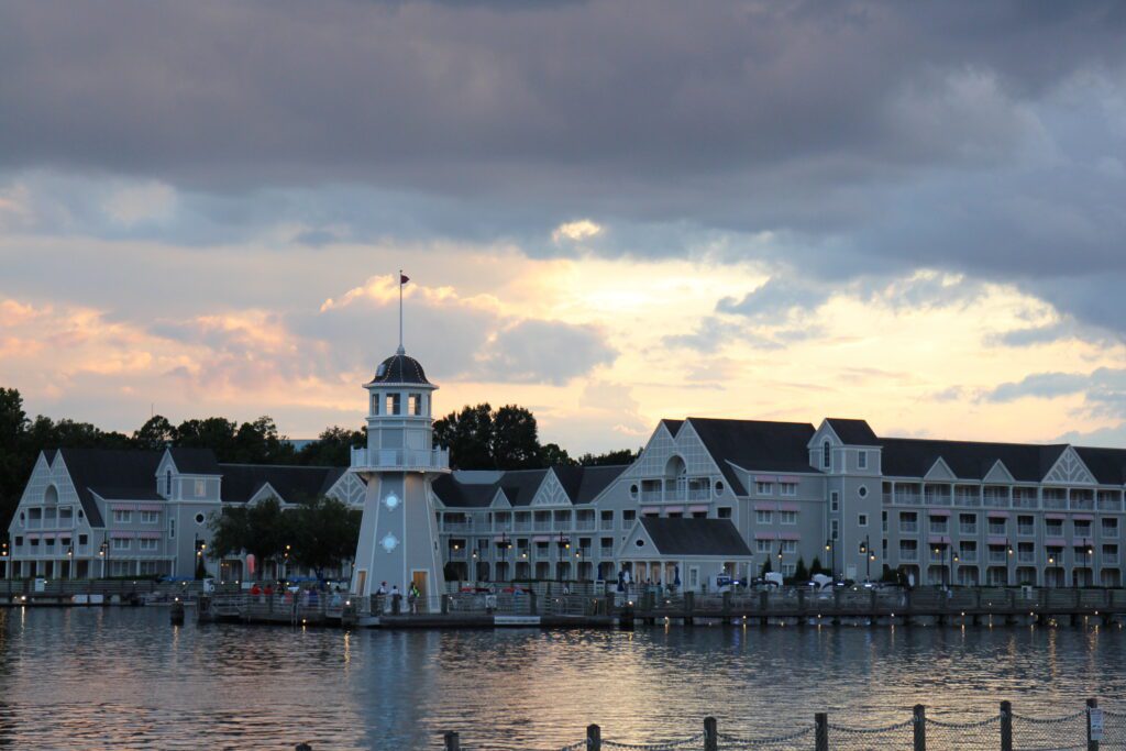 A sunset sky over the yacht club themed Disney resort with a dock and lighthouse.