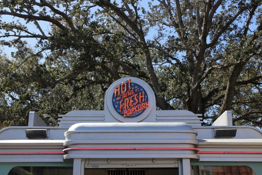 A vintage style popcorn kiosk with a neon sign that says "hot fresh popcorn."