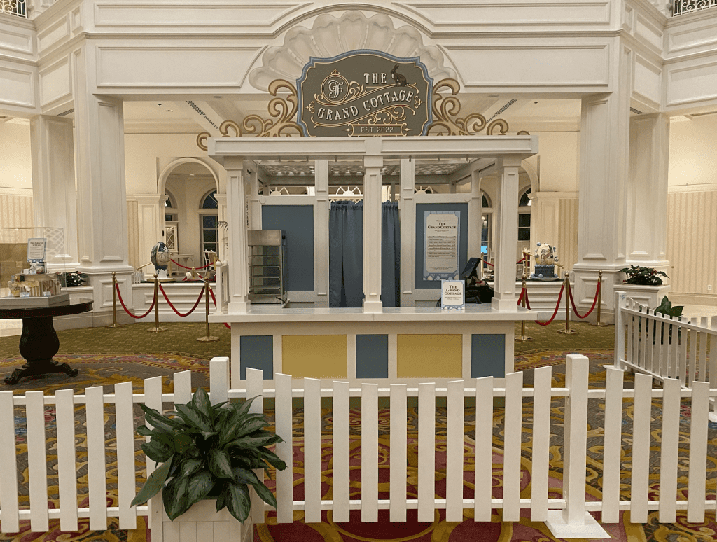 The Grand Cottage white, blue and yellow walk up treat kiosk in the Grand Floridian lobby. It's surrounded by a white picket fence.