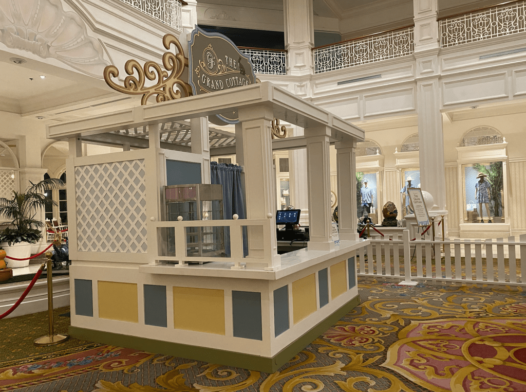 The Grand Cottage white, blue and yellow walk up treat kiosk in the Grand Floridian lobby. It's surrounded by a white picket fence.
