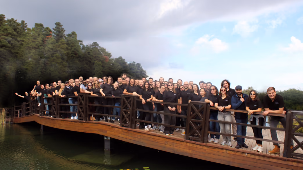 Wide group photo of Sestek employees on a wooden bridge over a lake
