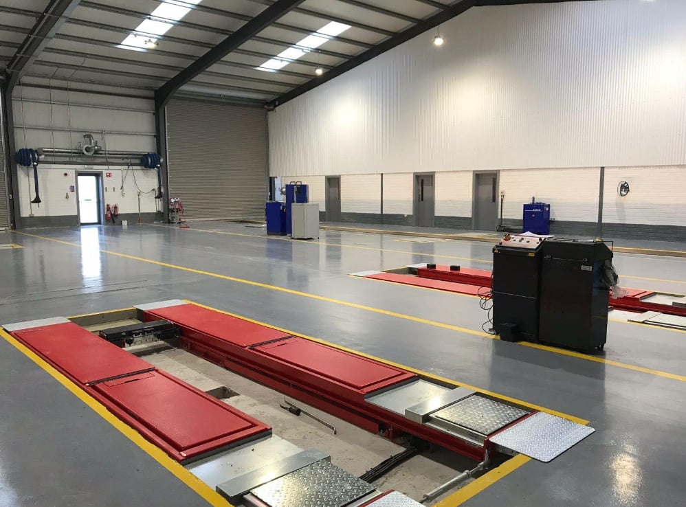 Empty vehicle inspection bay inside a clean, well-lit garage with red platforms and control equipment.