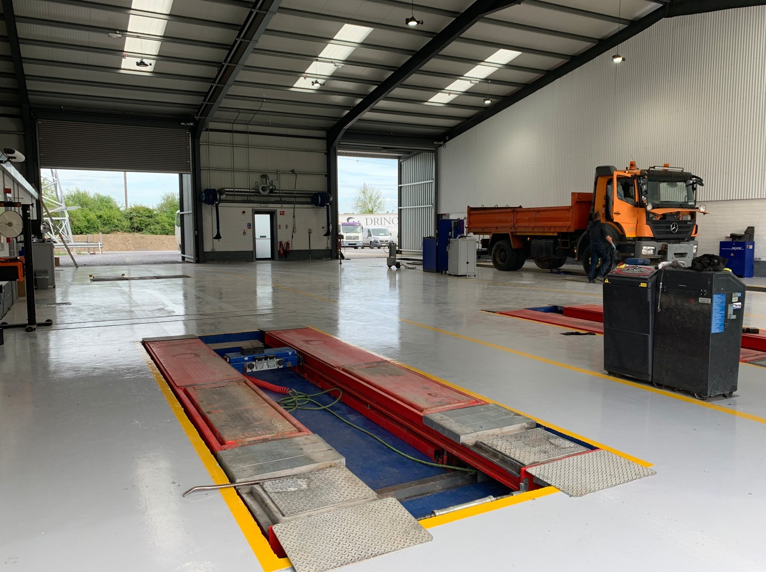 Interior of a large vehicle garage with inspection pits, an orange truck, and tools inside.