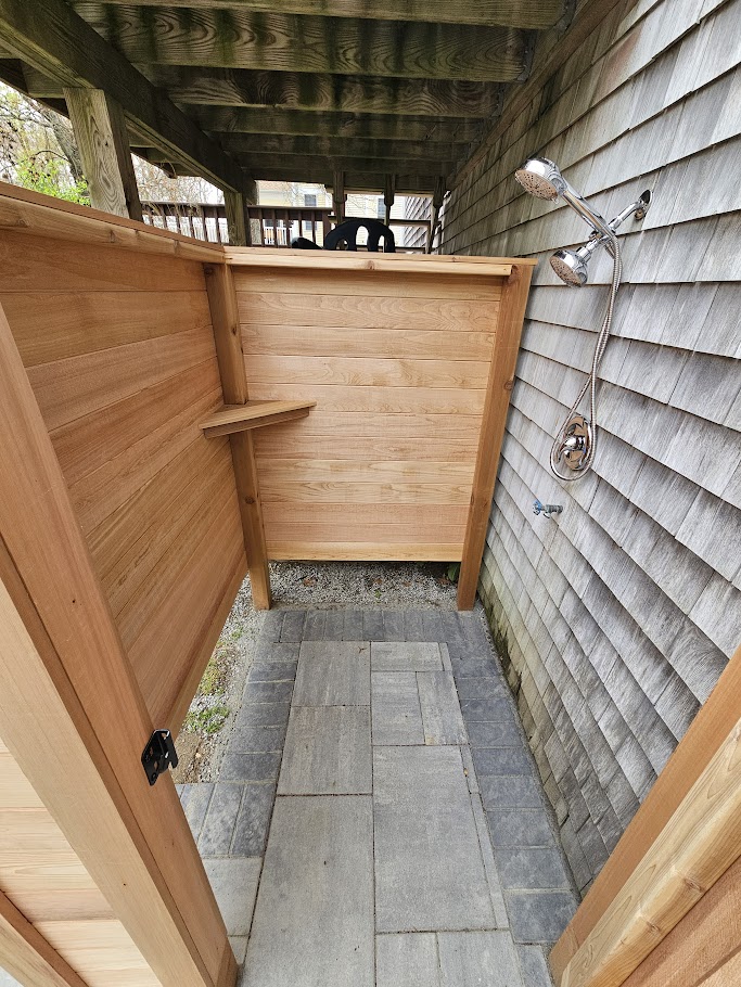 Clear cedar outdoor shower with louvered privacy wall and bluestone paver floor in Saunderstown, Rhode Island by Toensing Construction