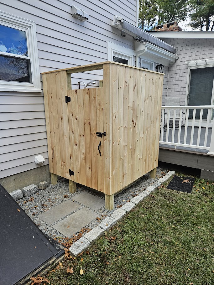 Custom freestanding outdoor shower with a slatted privacy door beside a home in Bristol, Rhode Island by Toensing Construction