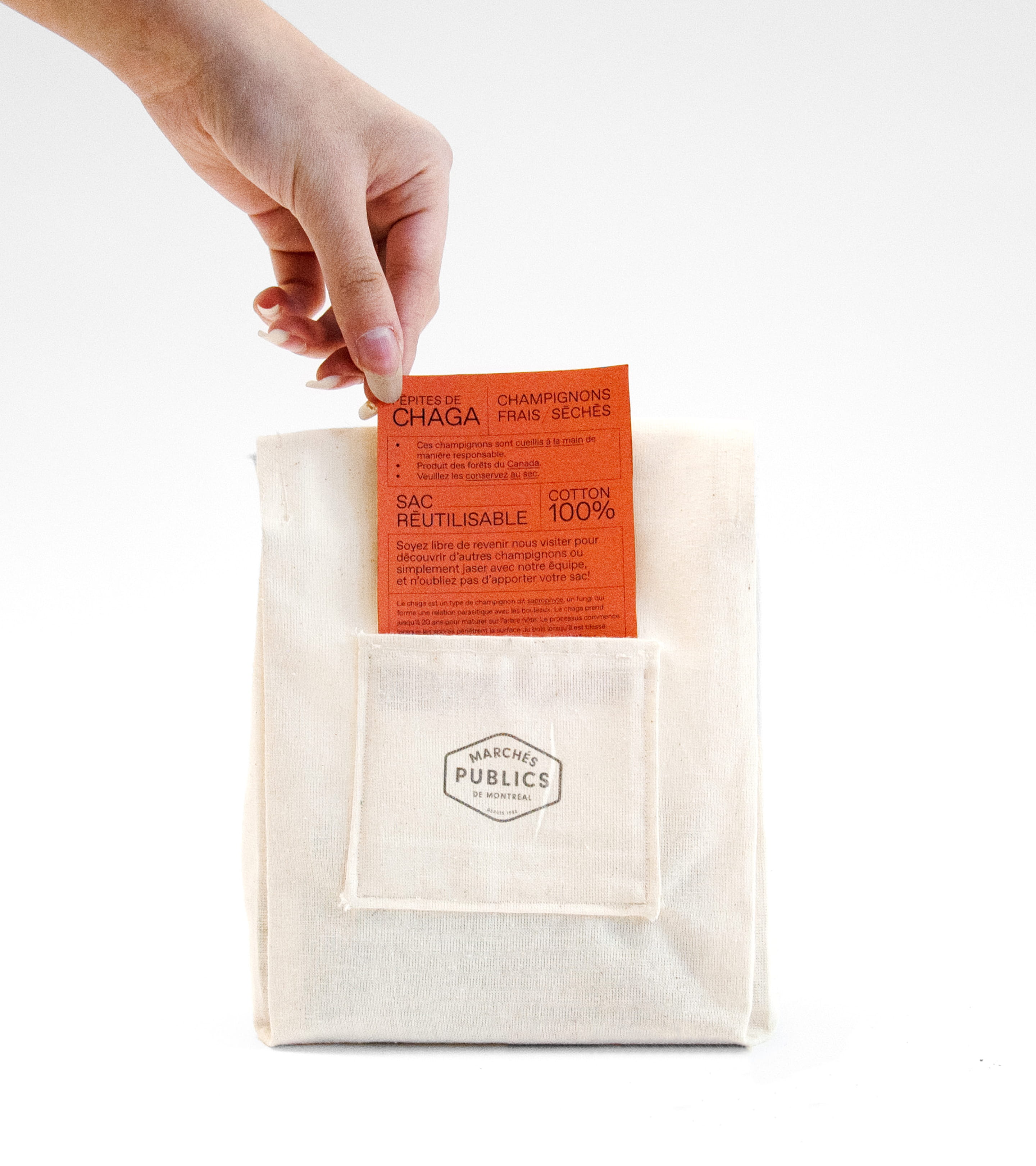 Shot of a hand taking a label card out of a textile bag with the Marchés Publics de Montréal logo on the pocket.