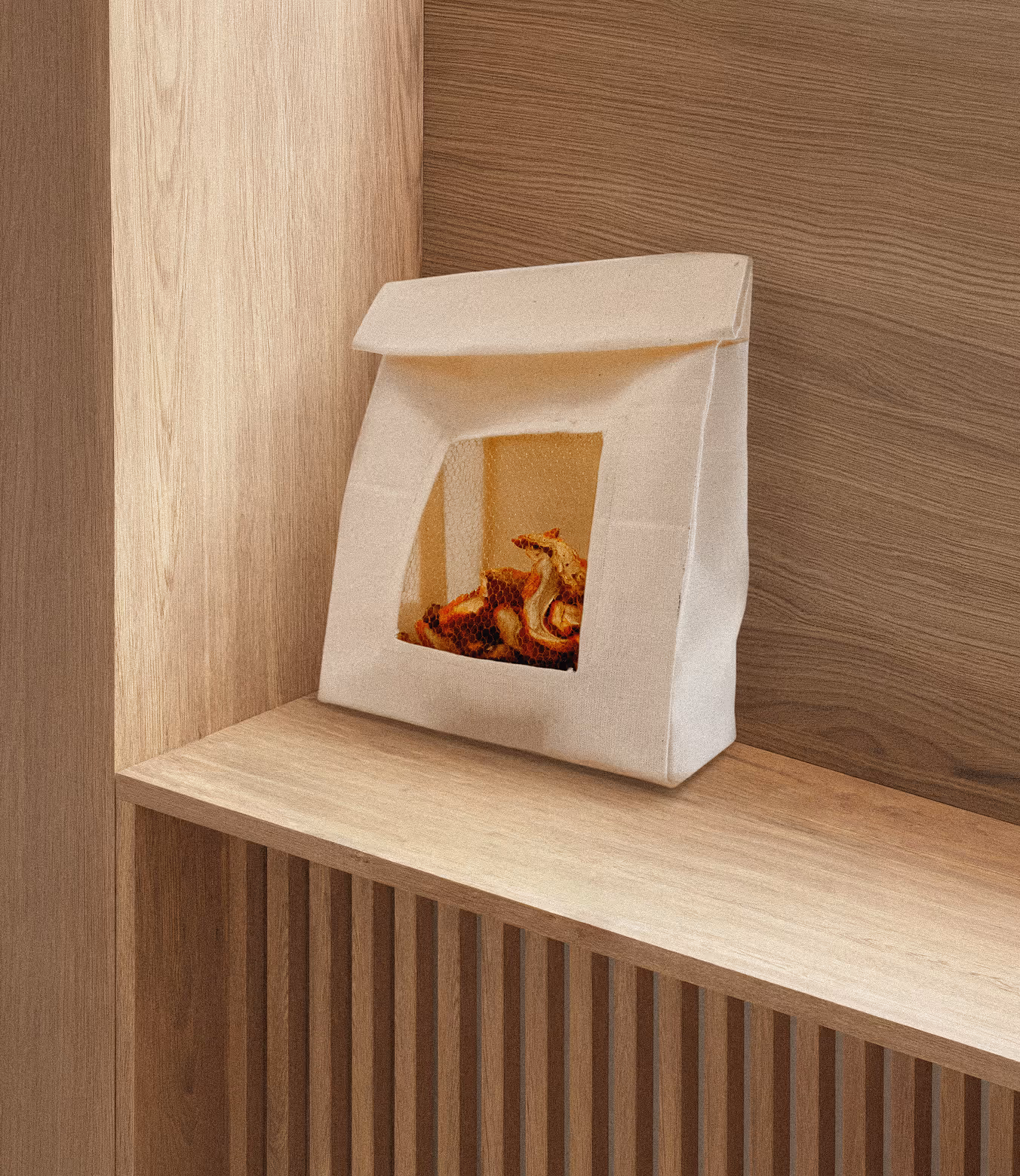 Cotton bag packaging lying on top of a wooden shelf. The front side has a small mesh window opening that showcases lobster mushrooms inside.