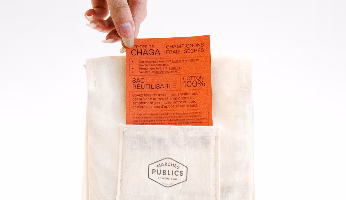 Shot of a hand taking a label card out of a textile bag with the Marchés Publics de Montréal logo on the pocket.