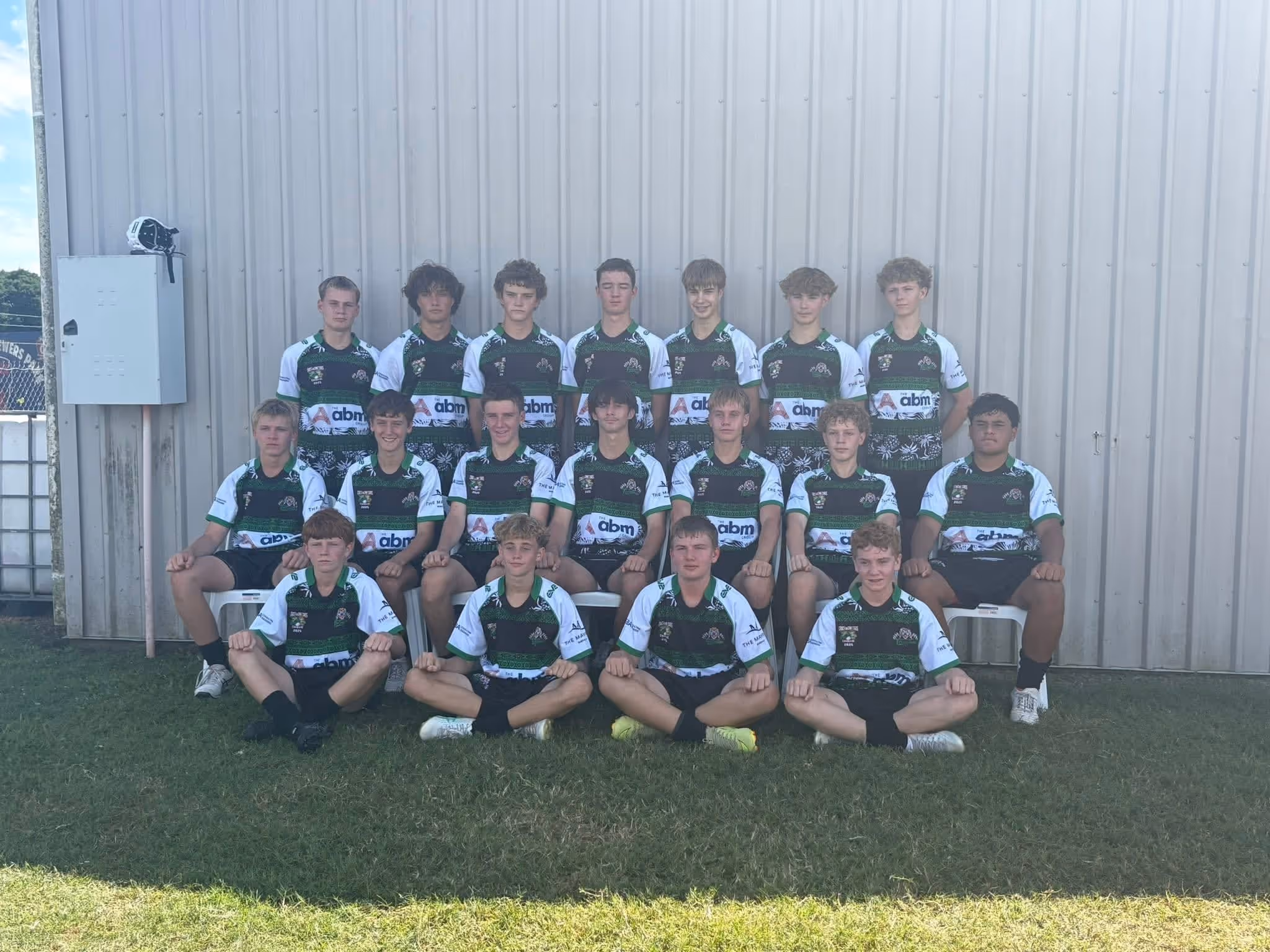 Group of teenage boys in green and white sports jerseys posing in front of a metal building.
