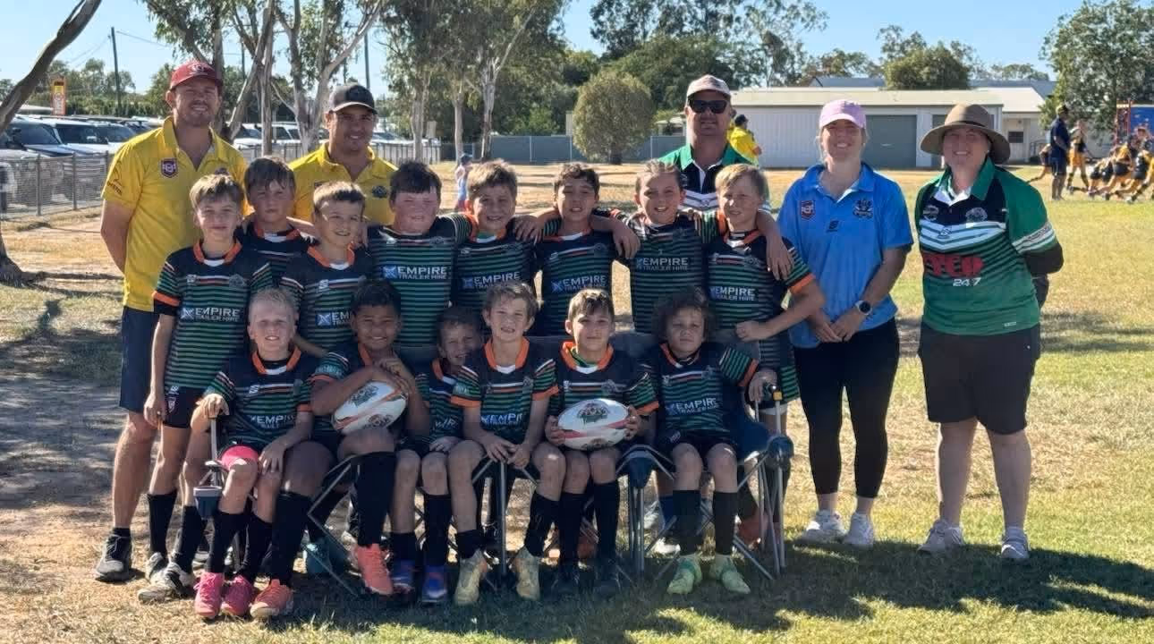 Youth rugby team in black and green uniforms posed with coaches outdoors on a sunny day.