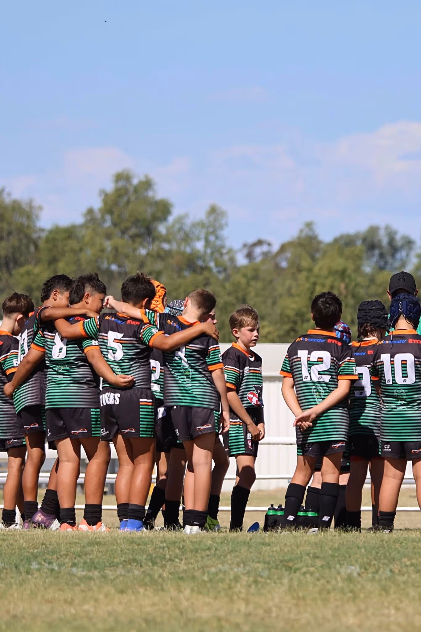Youth rugby players in green and black jerseys standing together on grass field outdoors.