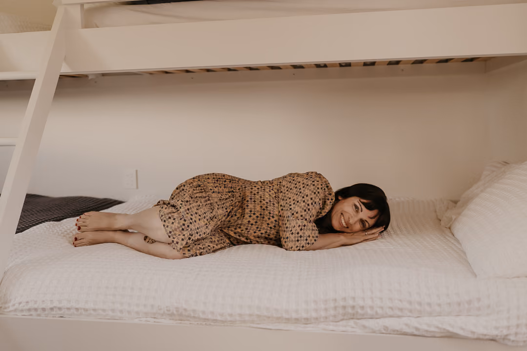 Coralie lying down on a bed with white sheets