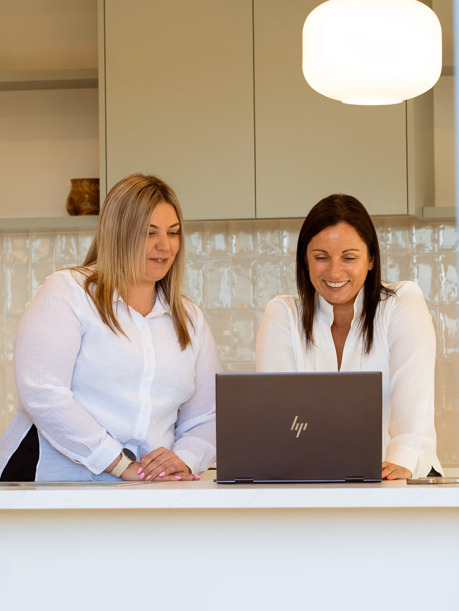 Coralie and Erica standing behind a counter looking at a laptop
