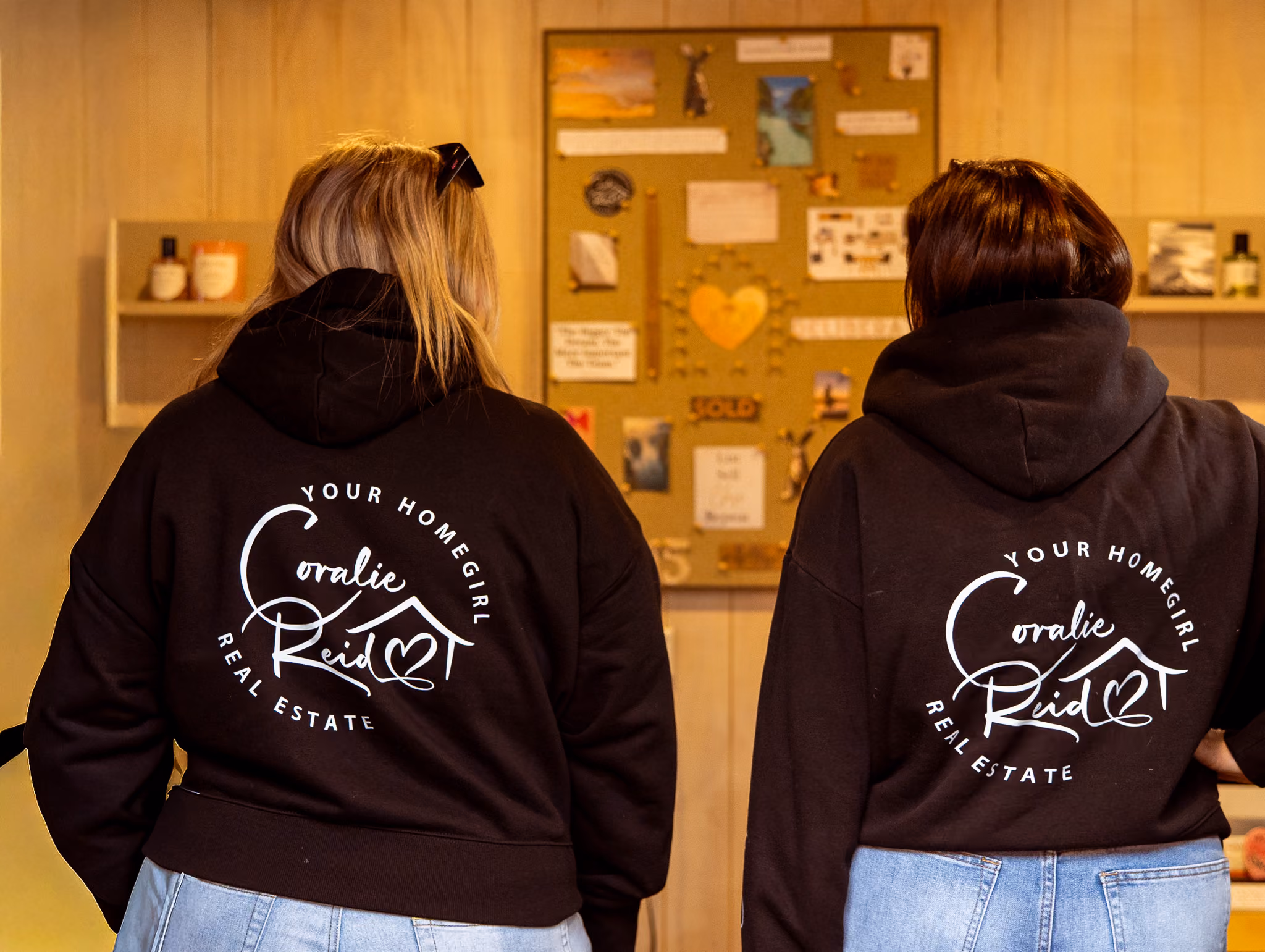 Coralie and Erica standing next to each other with their backs to the camera. Their jumpers have the Coralie real estate branding on it