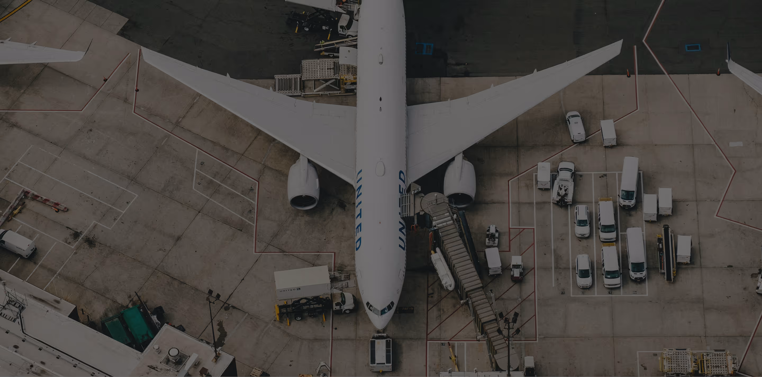 Top-down view of a United Airlines plane parked at an airport with ground service vehicles around it.