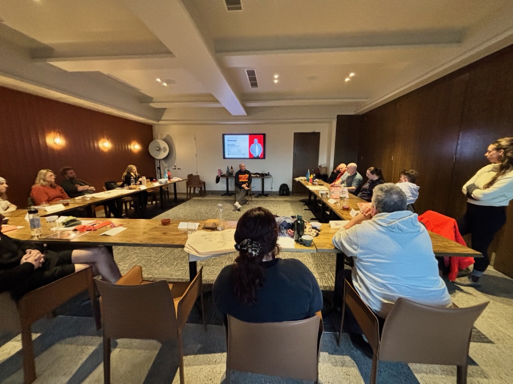 A Be BRAVE Feel SAFE session in a boardroom, participants around the table, Shawn Andrews facilitating at the front