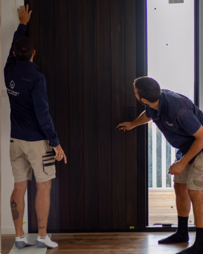 Two men inspecting a dark wooden door in a modern interior space with hardwood flooring.