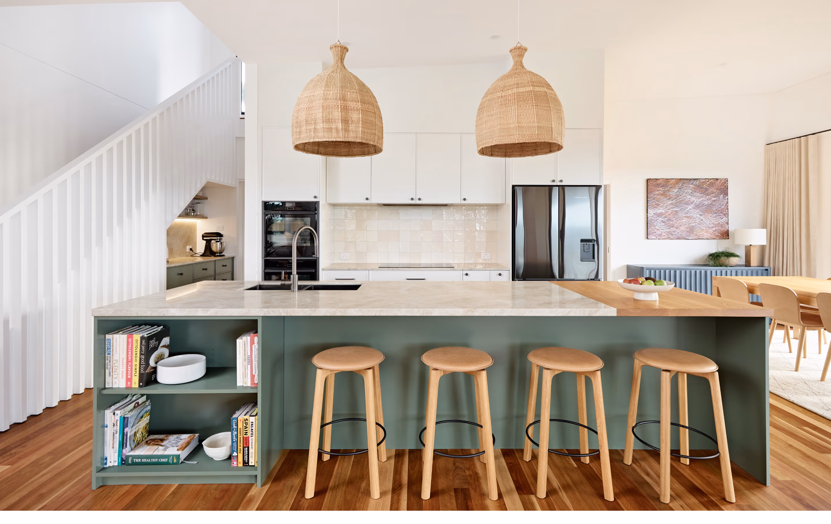 Modern kitchen with green island, wooden stools, two wicker pendant lights, and stainless steel appliances.