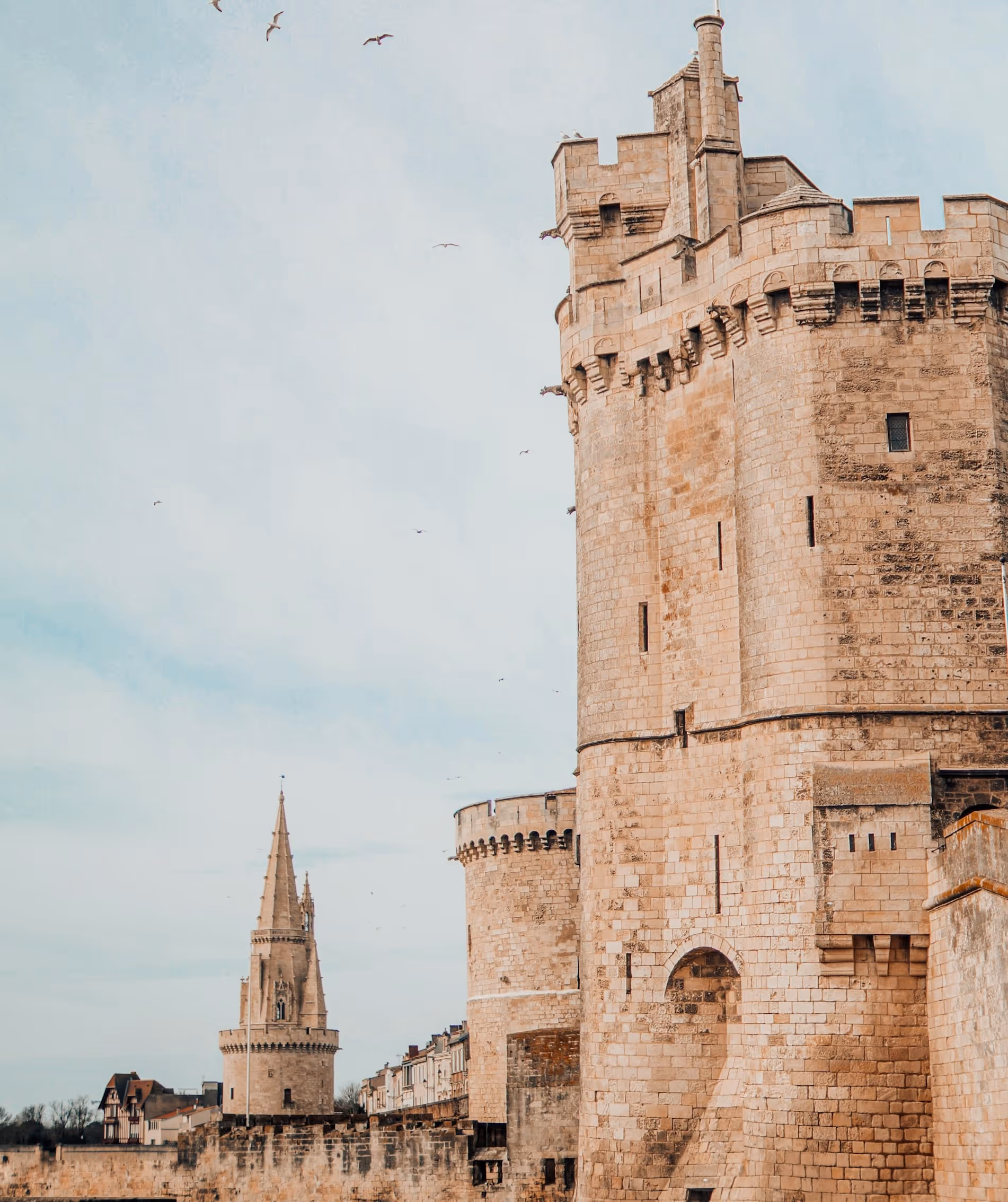 Vue des tours en pierre historiques et des maisons derrière un vieux mur sous un ciel bleu clair.