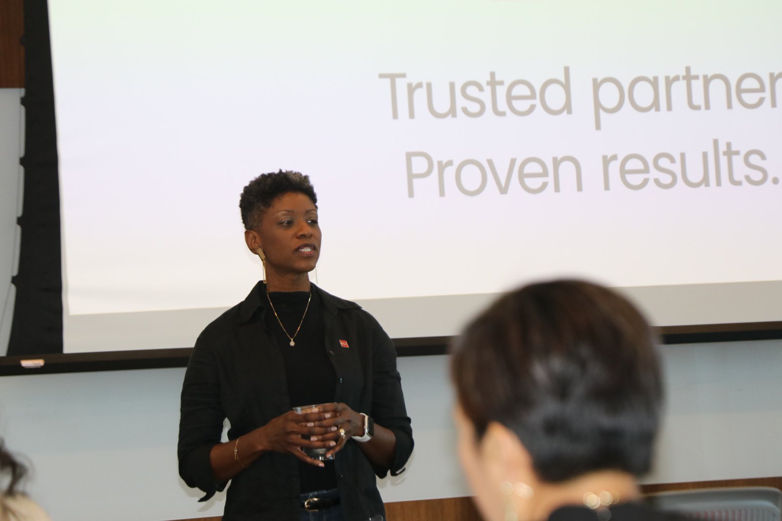 Woman presenting to audience with corporate slide behind her