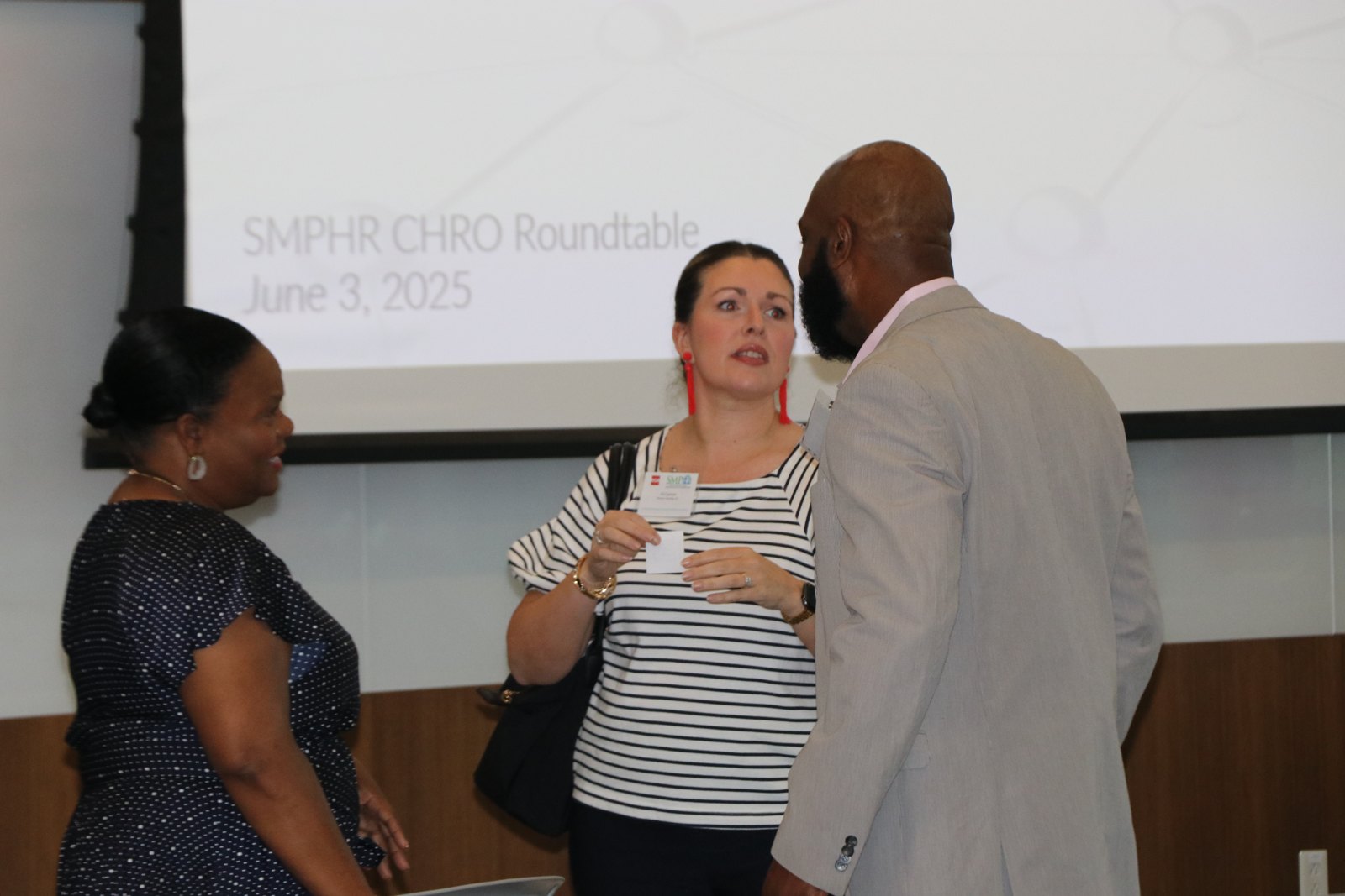 Three professionals conversing at CHRO Roundtable event with projected slide