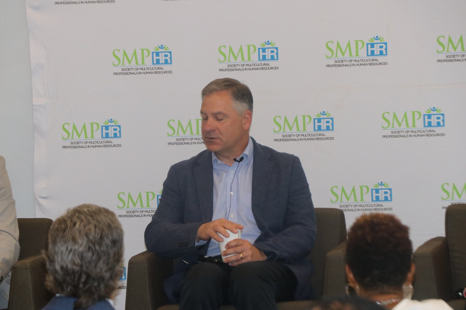 Man in blue shirt speaking at professional panel with SMPHR backdrop