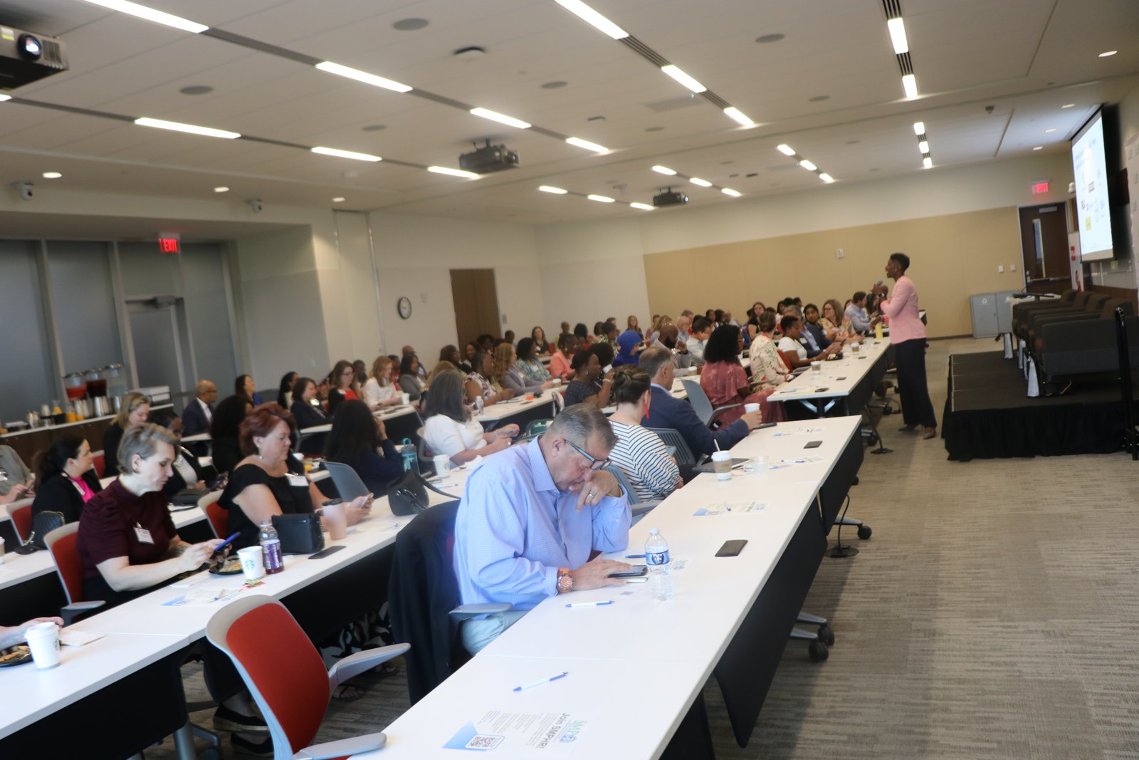 Large workshop with many attendees seated at tables and presenter