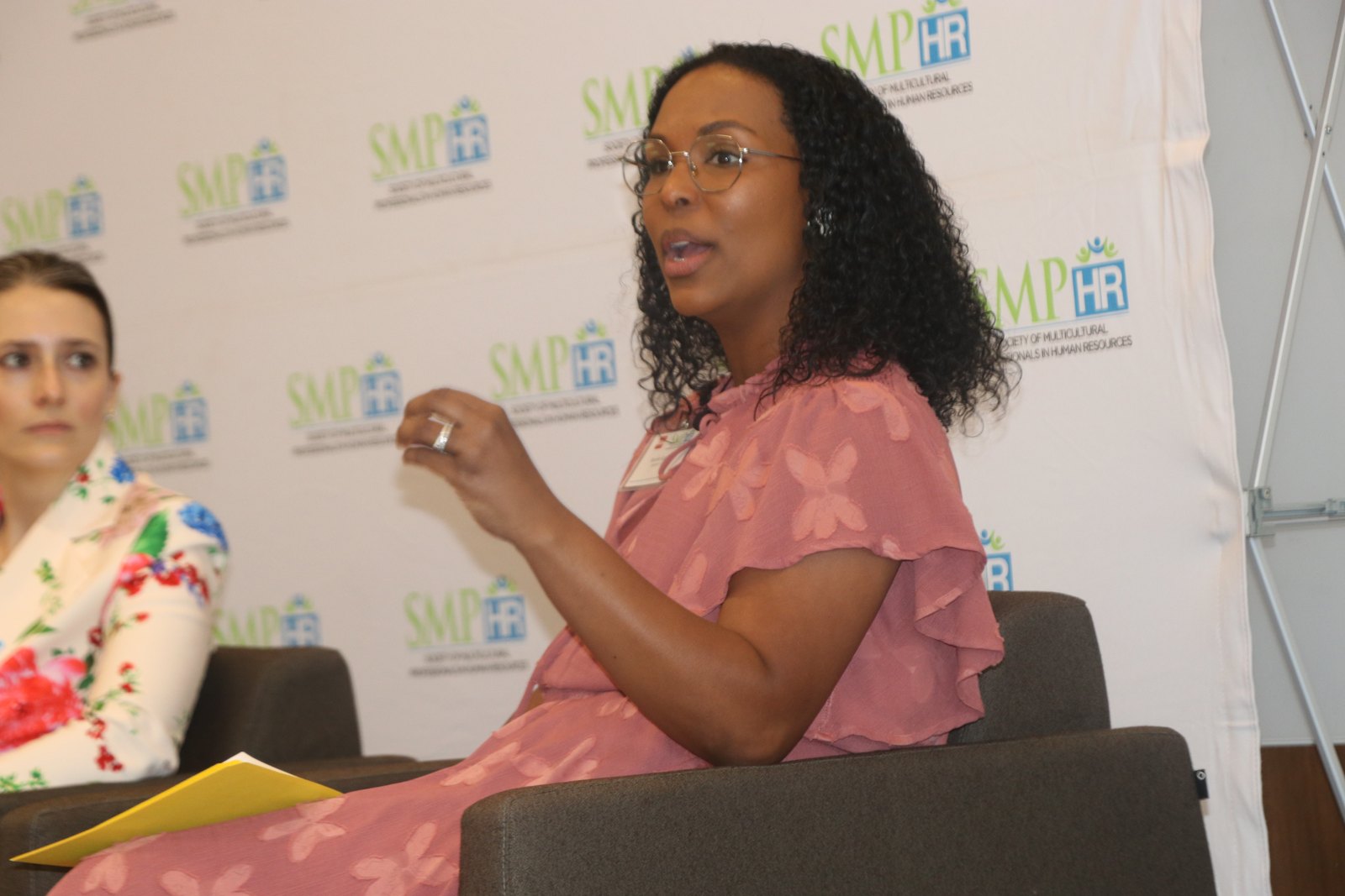Woman in coral top speaking at SMPHR panel with backdrop