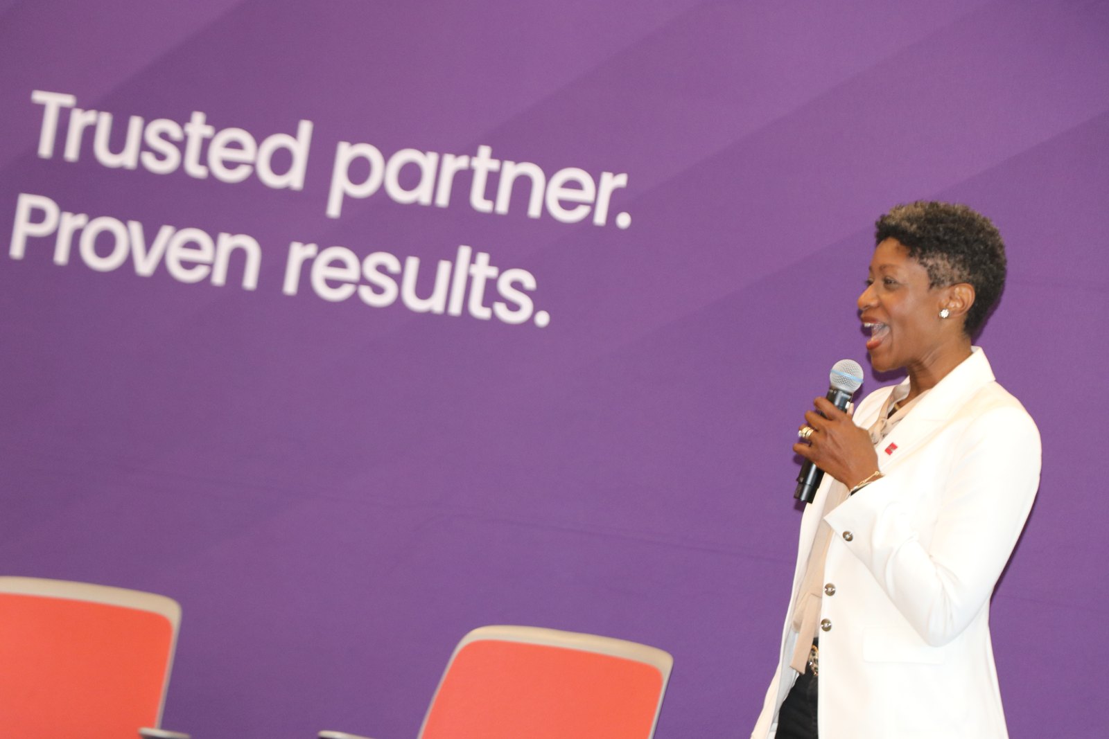 Woman speaking at podium with RGA logo and purple branded backdrop