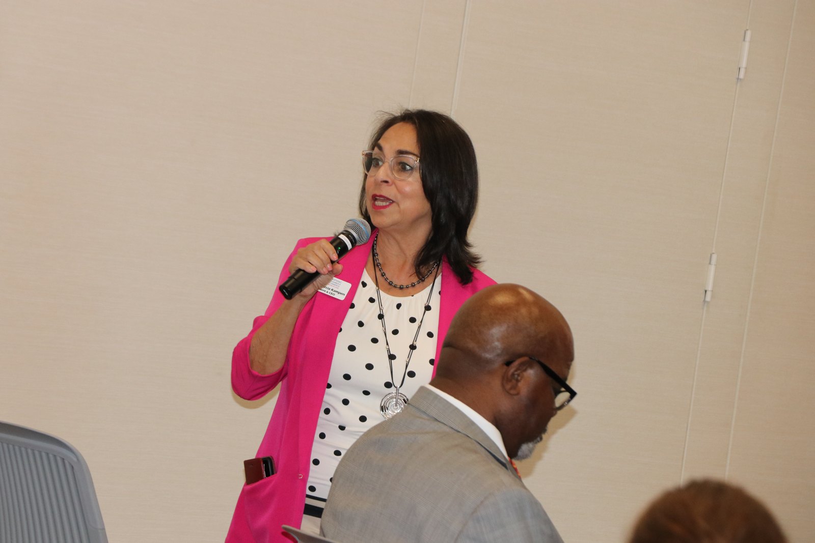 Woman in bright pink blazer speaking at microphone with SMPHR logo in background