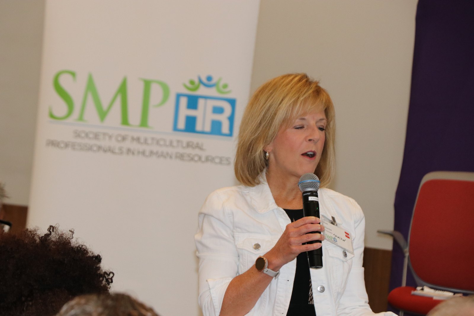 Woman in white jacket at microphone with SMPHR branding in background