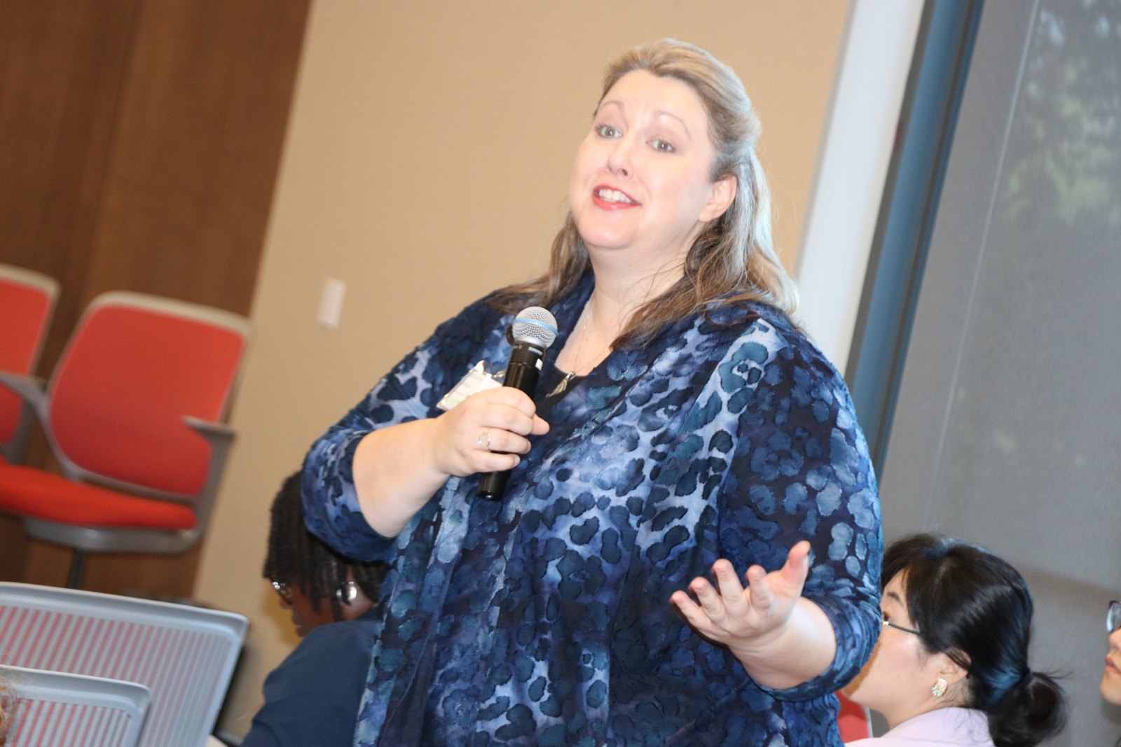 Woman in leopard print jacket gesturing while speaking at microphone