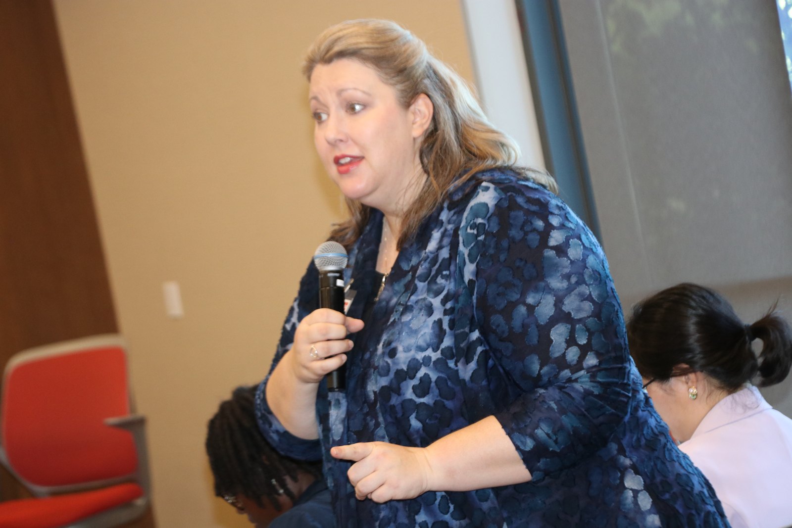 Woman in leopard print jacket speaking with audience members visible in background