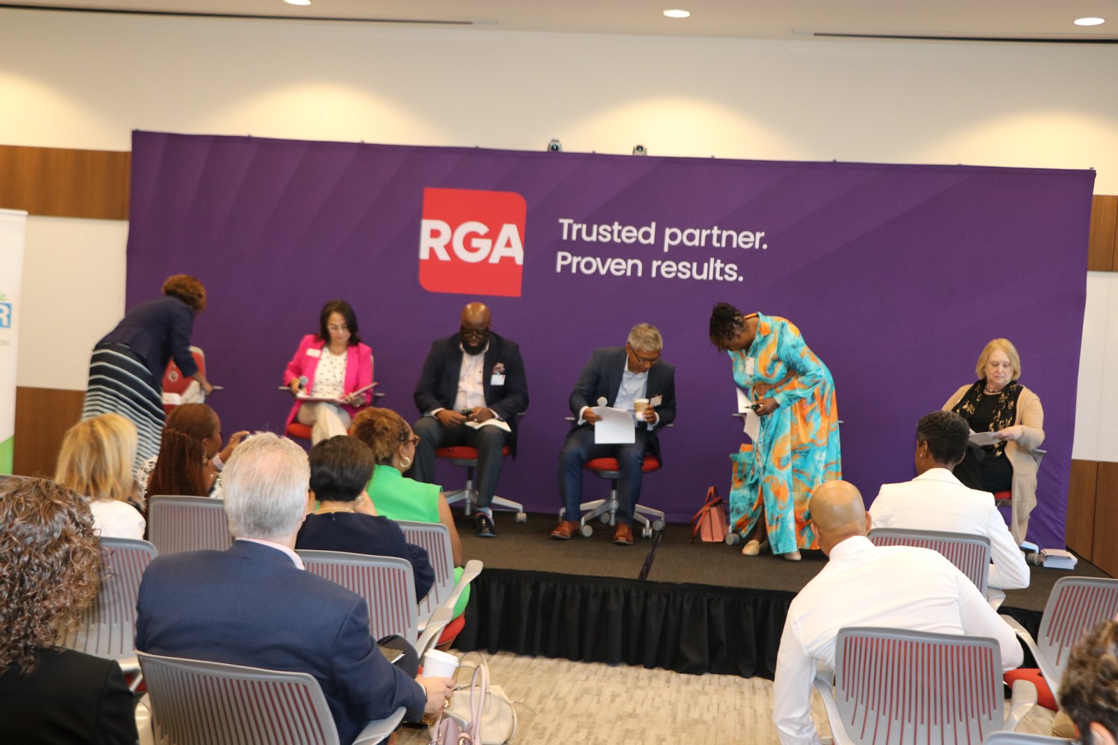 Six HR professionals in panel discussion against purple RGA backdrop, with audience seated in foreground