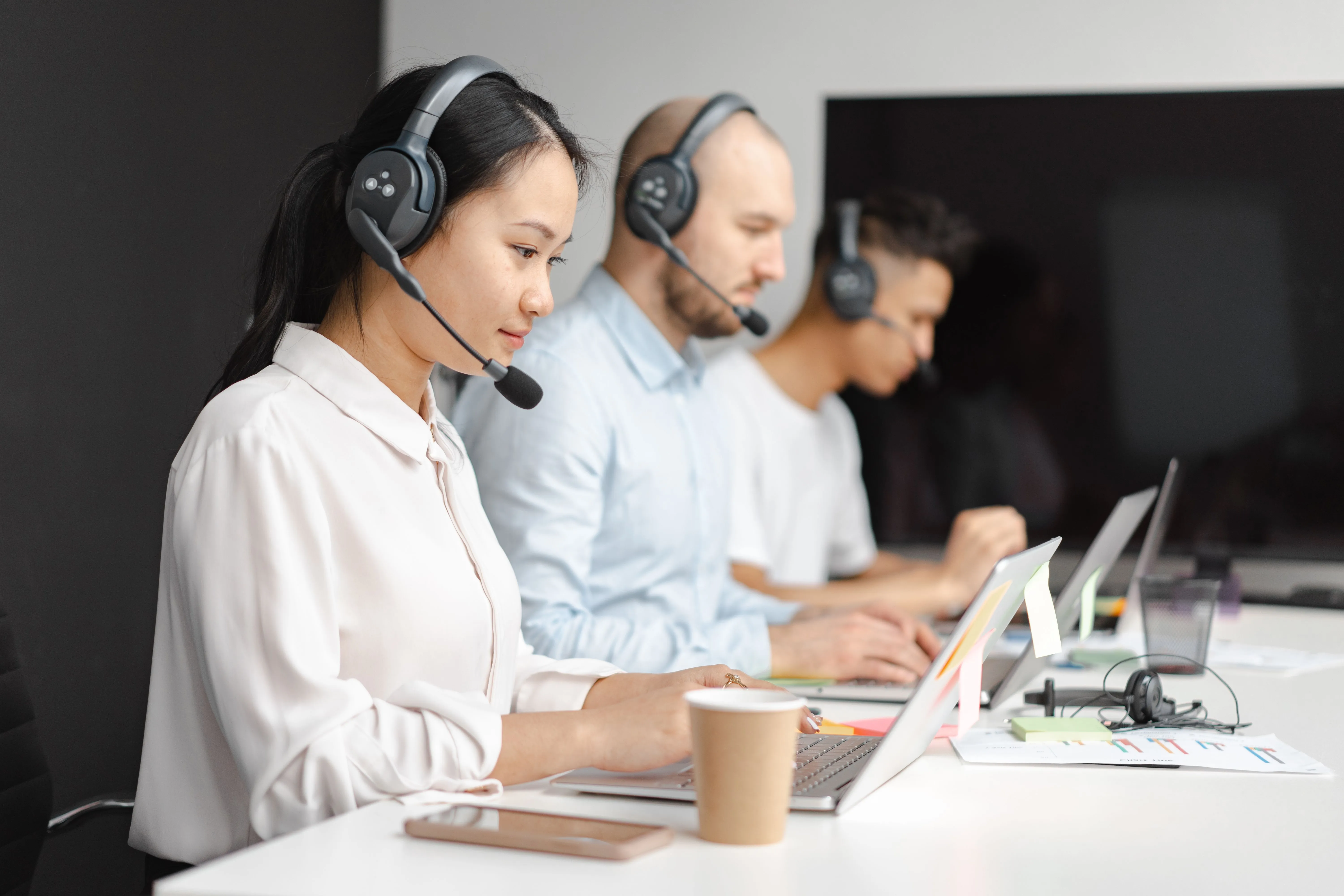 Trois téléconseillers avec casque, travaillant sur ordinateur portable en open space.