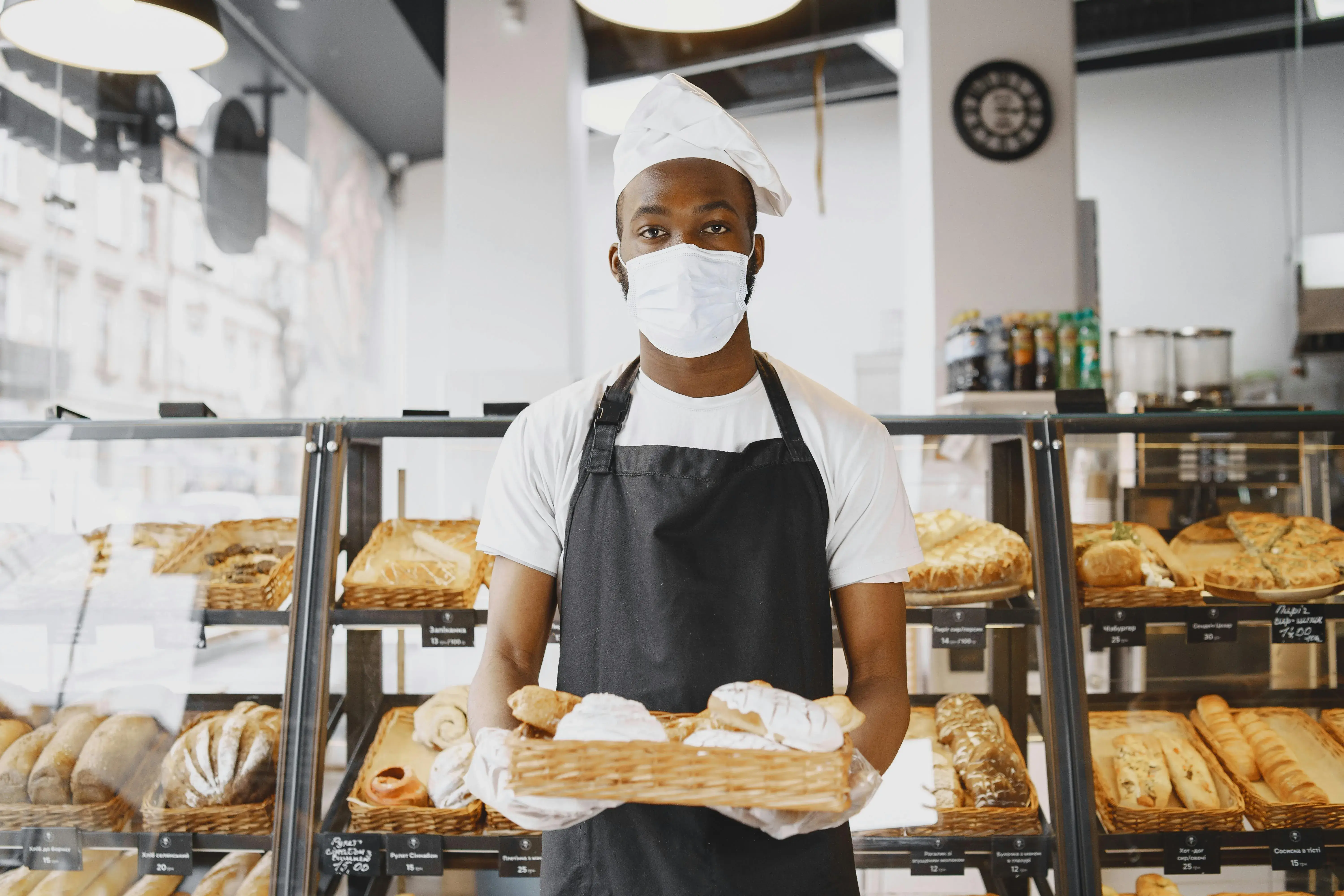 Boulanger portant charlotte et masque, présentant un panier de pains et viennoiseries.