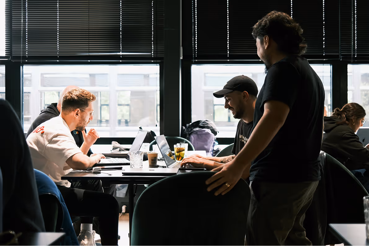 People working on laptops in a modern office with large windows and blinds.