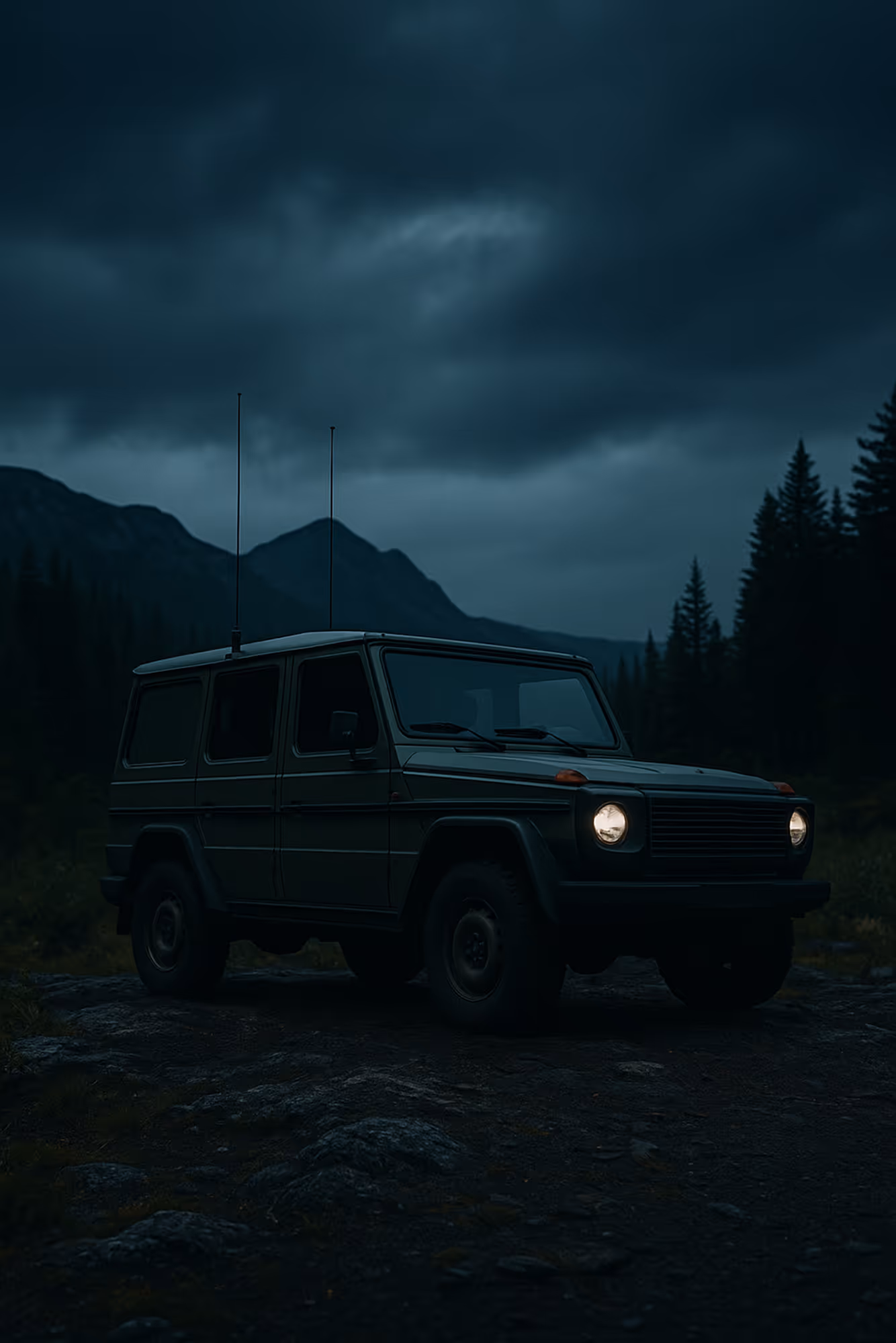 Dark green off-road SUV with headlights on, parked on rocky ground in forested mountains at dusk.