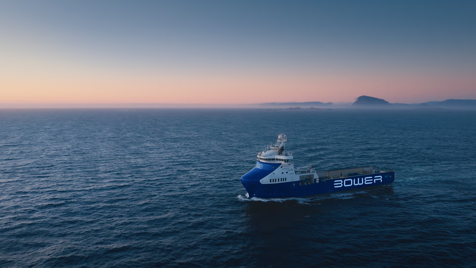 Bower Eir sailing on calm ocean waters at sunset with distant land on the horizon.