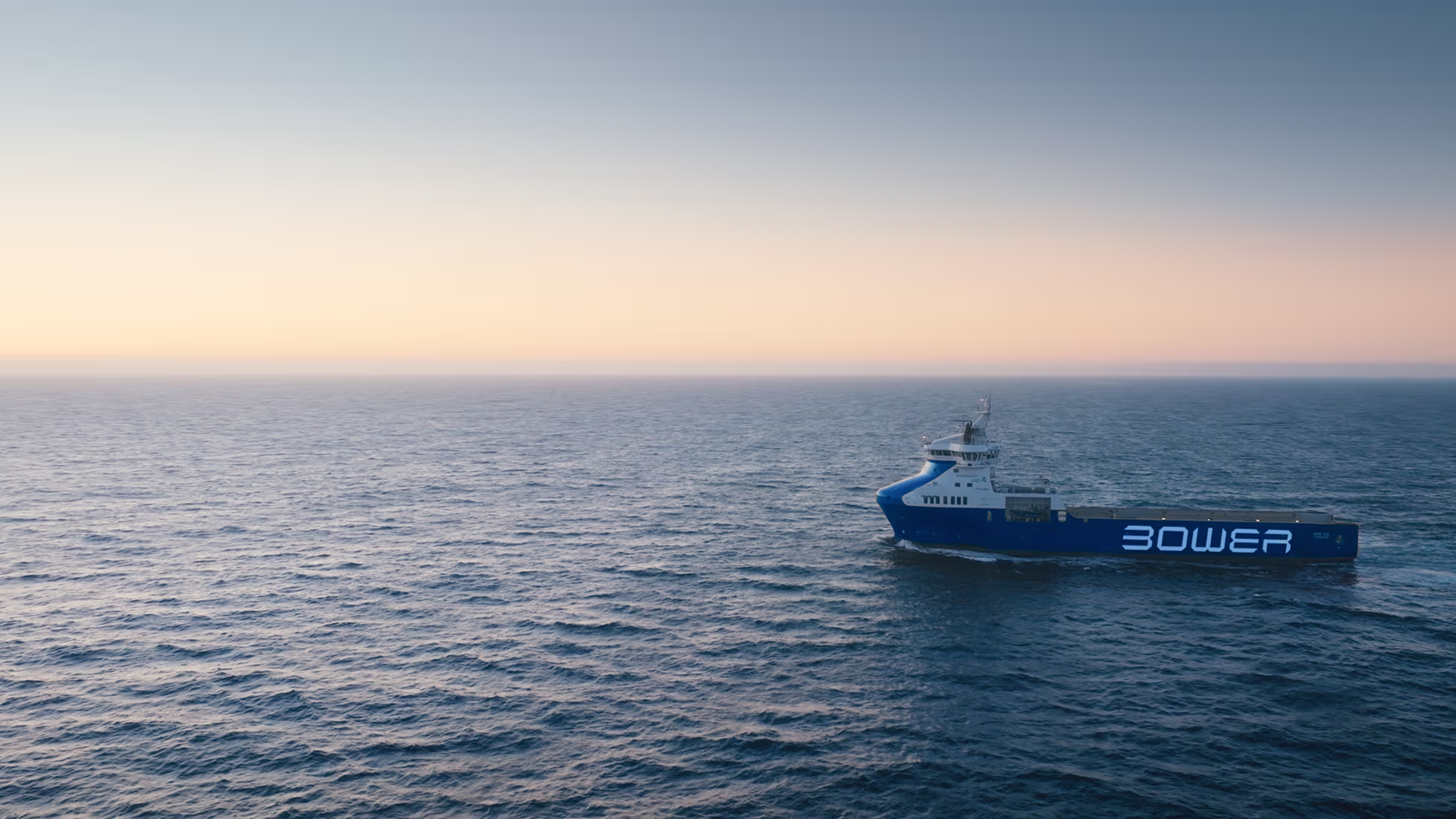 Bower Eir sailing on calm ocean waters at sunset with distant land on the horizon.
