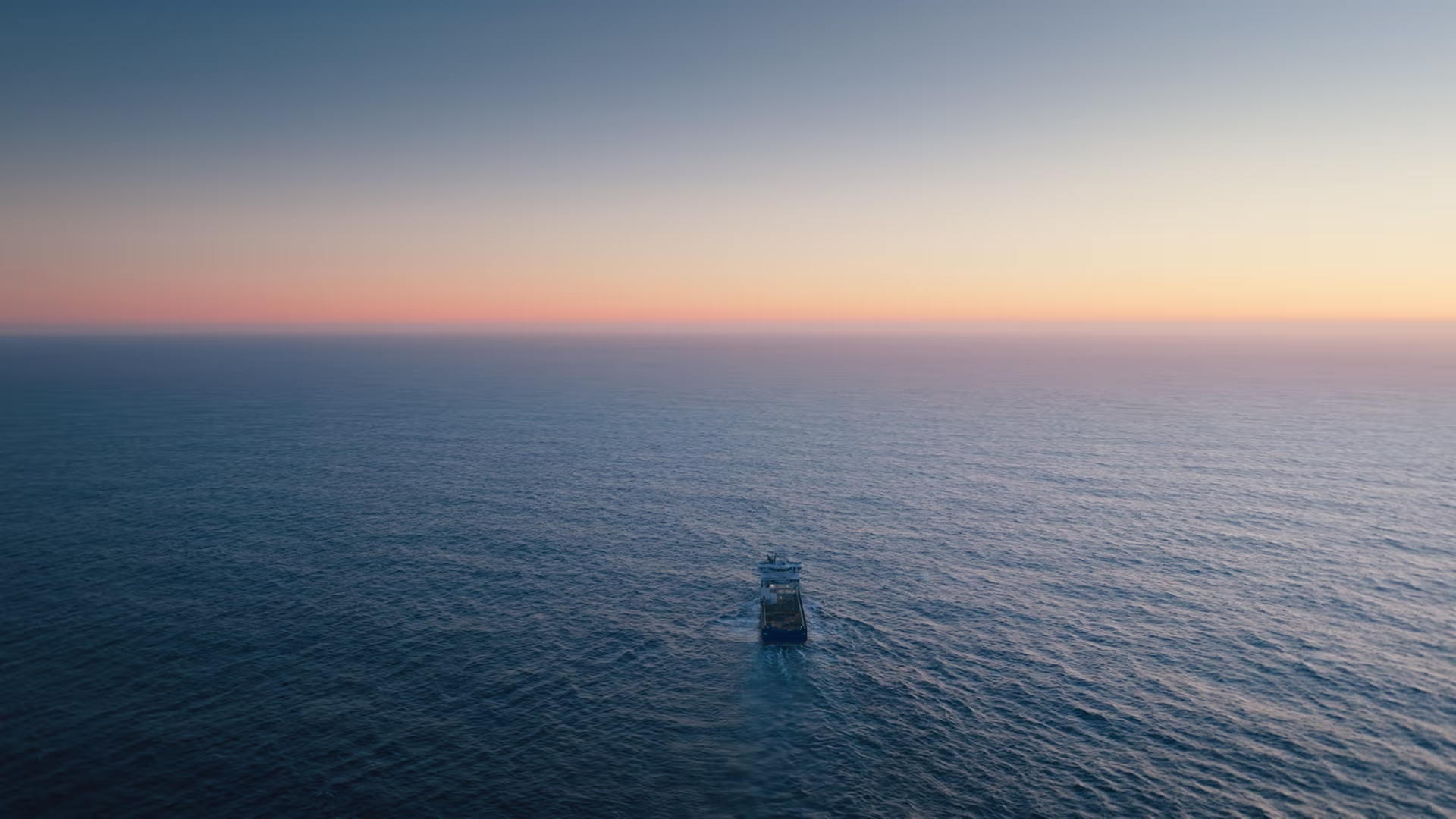 Bower Eir sailing on calm ocean waters at sunset with distant land on the horizon.
