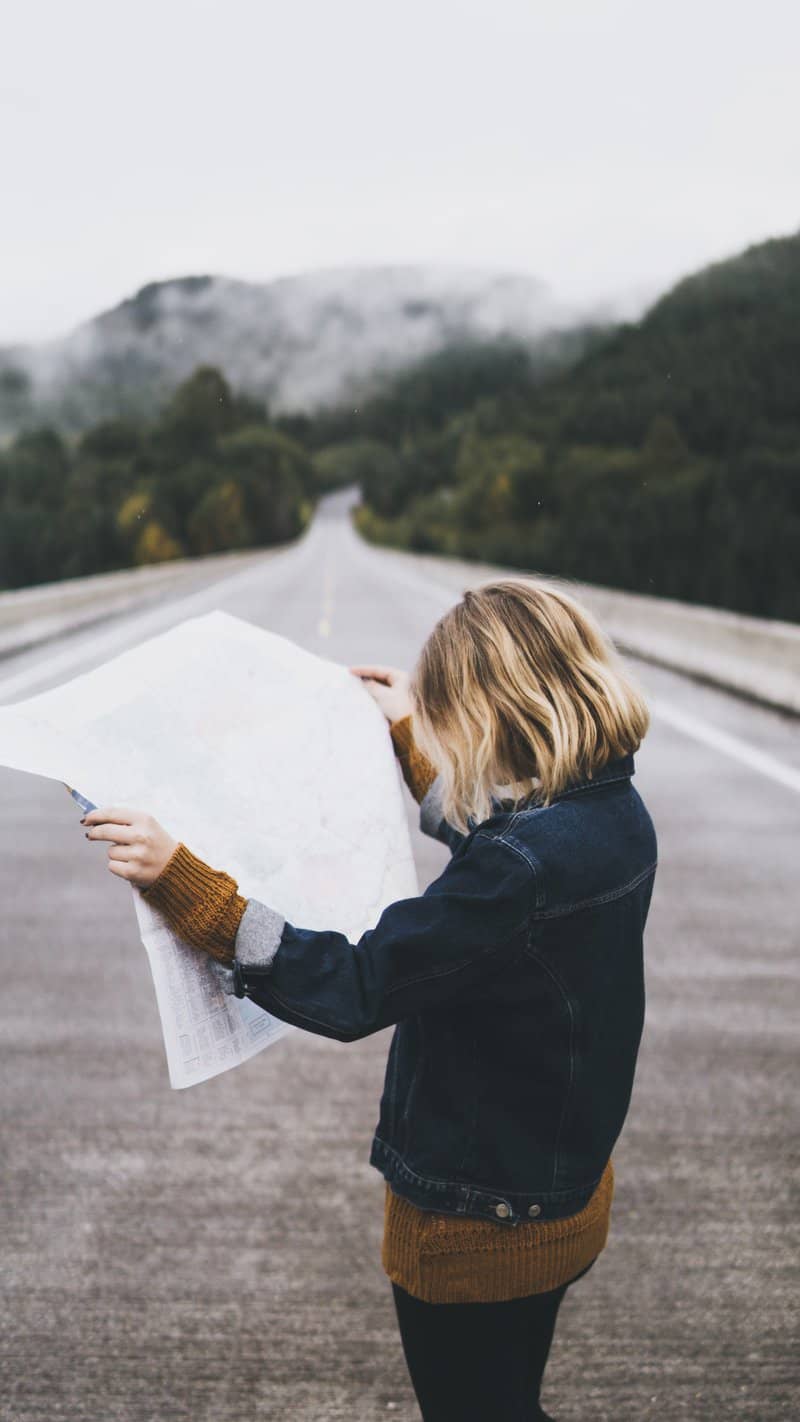 Image d’une femme consultant une carte au milieu d’une route