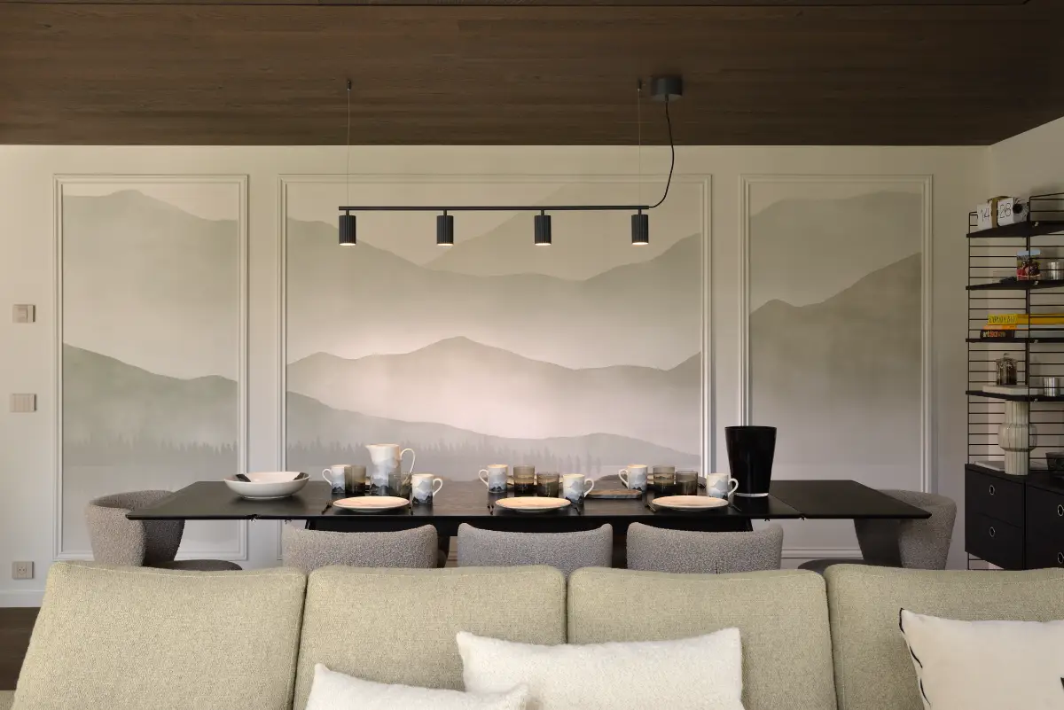 Villa g, intérieur salon vue salle à manger, avec une grande table dressée devant un mur orné de cadre représentants des montagnes en filigrane