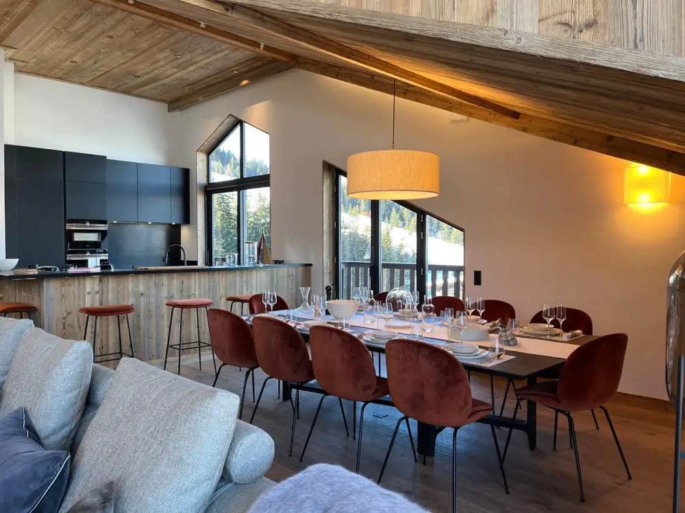 Appartement D, Courchevel, intérieur vue cuisine avec une grande table conviviale dressée au premier plan et le mobilier cuisine en arrière plan