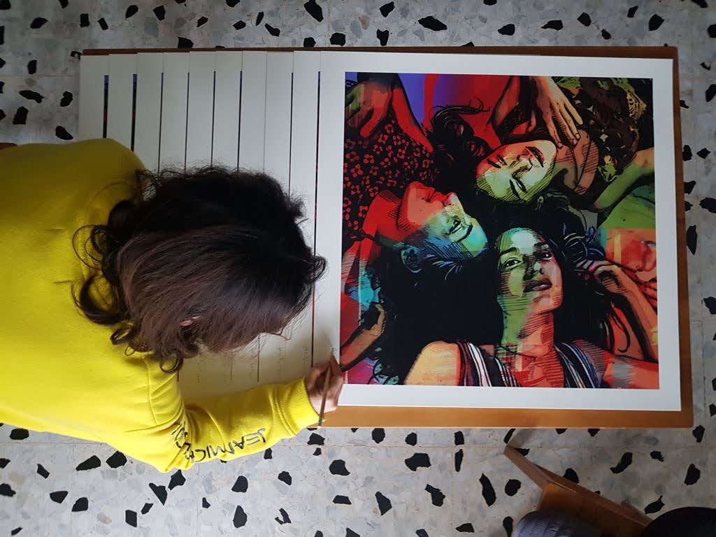 Alice Pasquini signing Teen Spirit, seen from above, the numbered stack of prints fanned out beside the finished sheet