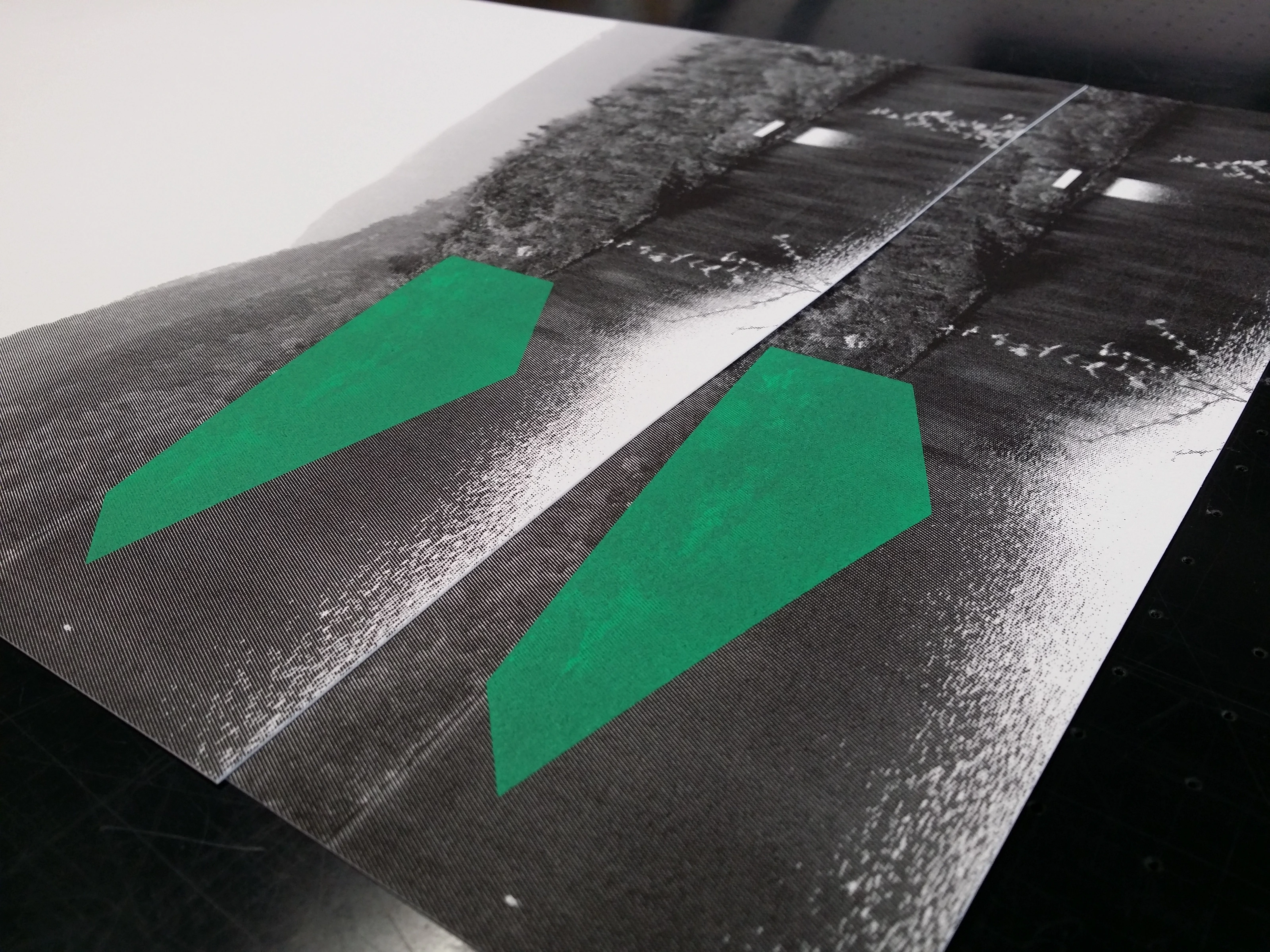 Detail of Amy Stephens' The Lookout — two screenprints on a studio table showing the green shape over halftone forest.