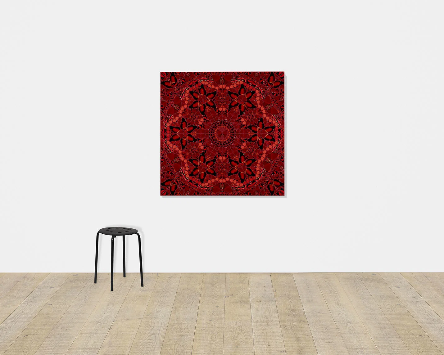 Damien Hirst's Wu Zetian, a large red kaleidoscopic butterfly print, hangs on a white gallery wall above a black stool.