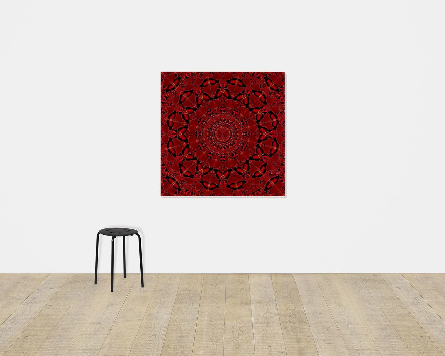 Damien Hirst's Suiko, a large red kaleidoscopic butterfly print, hangs on a white gallery wall above a black stool.