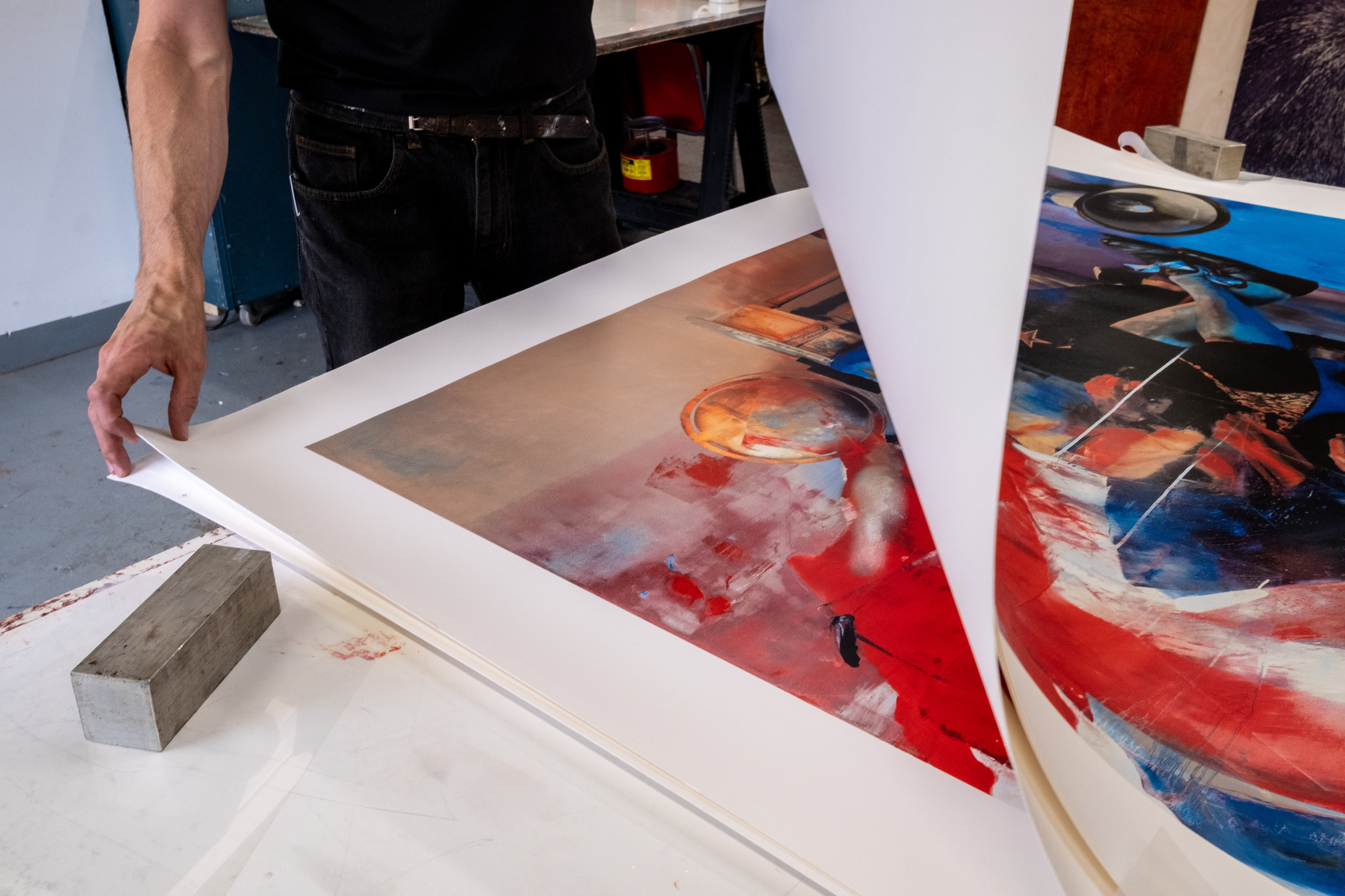 A printer lifts the corner of Conor Harrington's The Blind Exit on a studio bench, checking the red, blue and orange print beneath.
